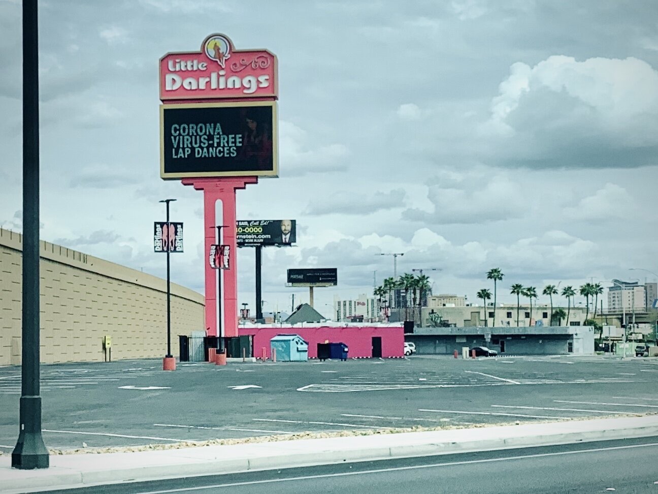 Roadside sign for the Little Darlings club advertising corona virus-free lap dances above an empty parking lot.